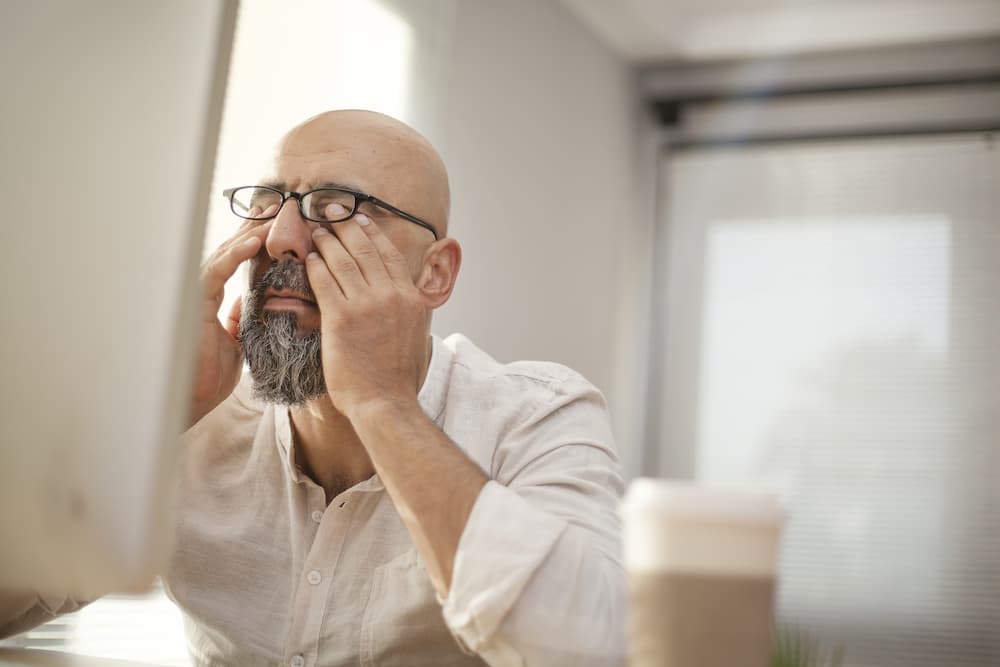 Older guy rubbing his eyes in front of a computer
